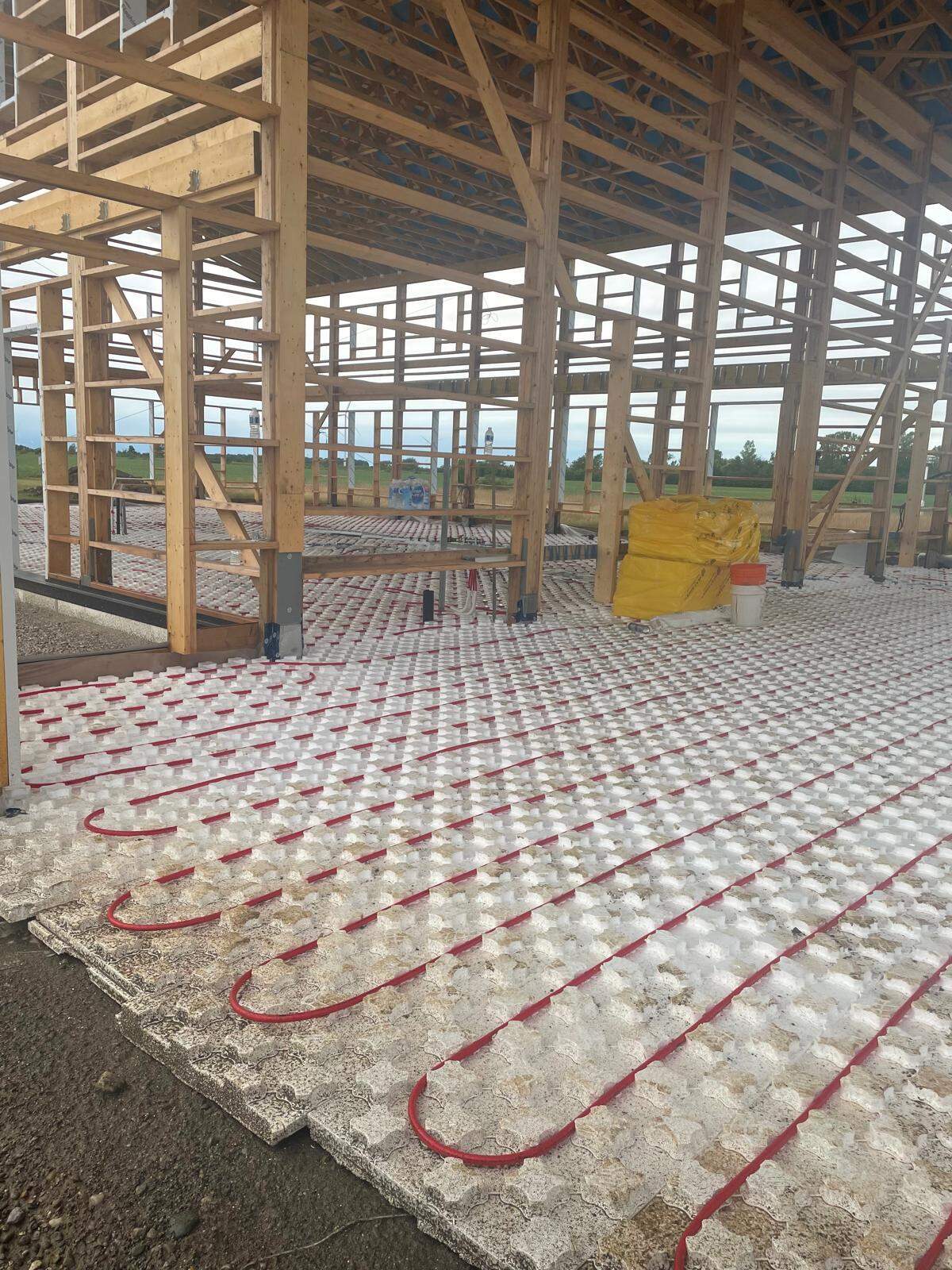 Post-frame barndominium construction showing timber framing with radiant floor system before slab pour